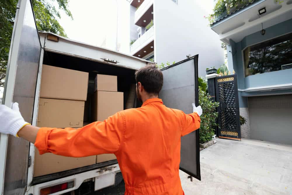 Removalist opening a truck to load packed cardboard boxes outside a residential property.